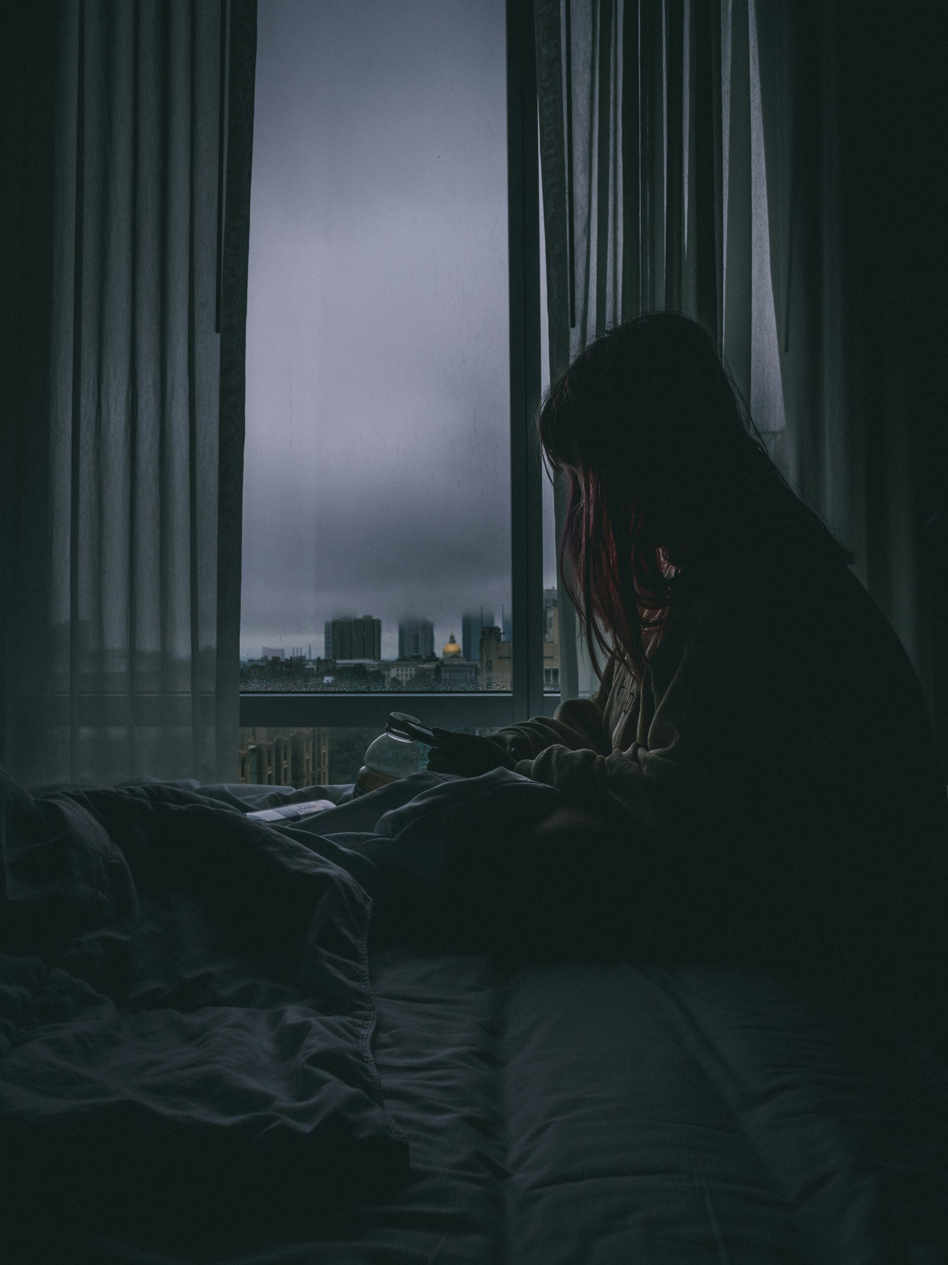 “A woman sitting alone on bed near a window during evening, lost in thoughts – symbolic of sunset anxiety and overthinking.”
