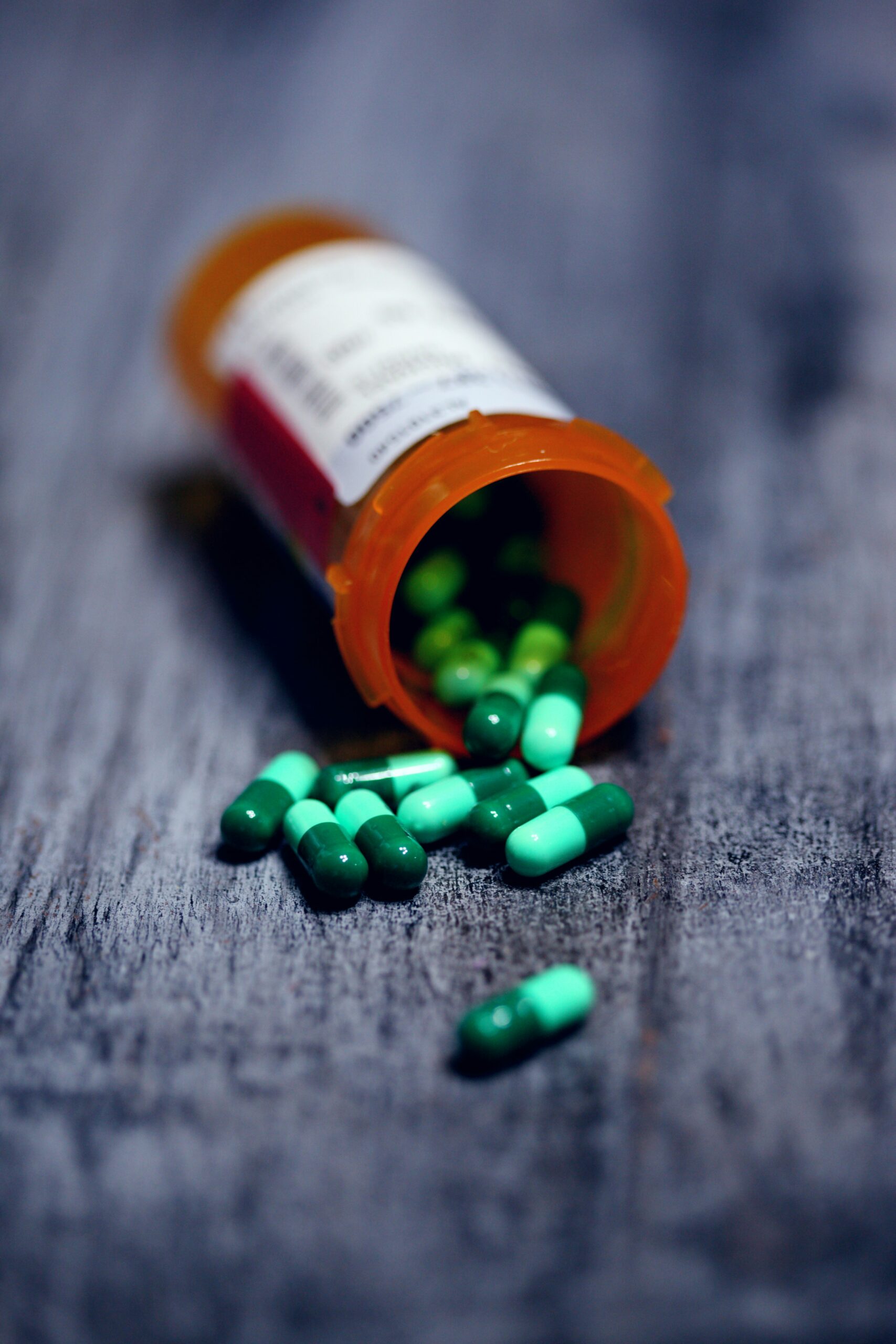 “Green and teal capsules spilling from an orange prescription bottle onto a wooden surface, representing anxiety medication.”