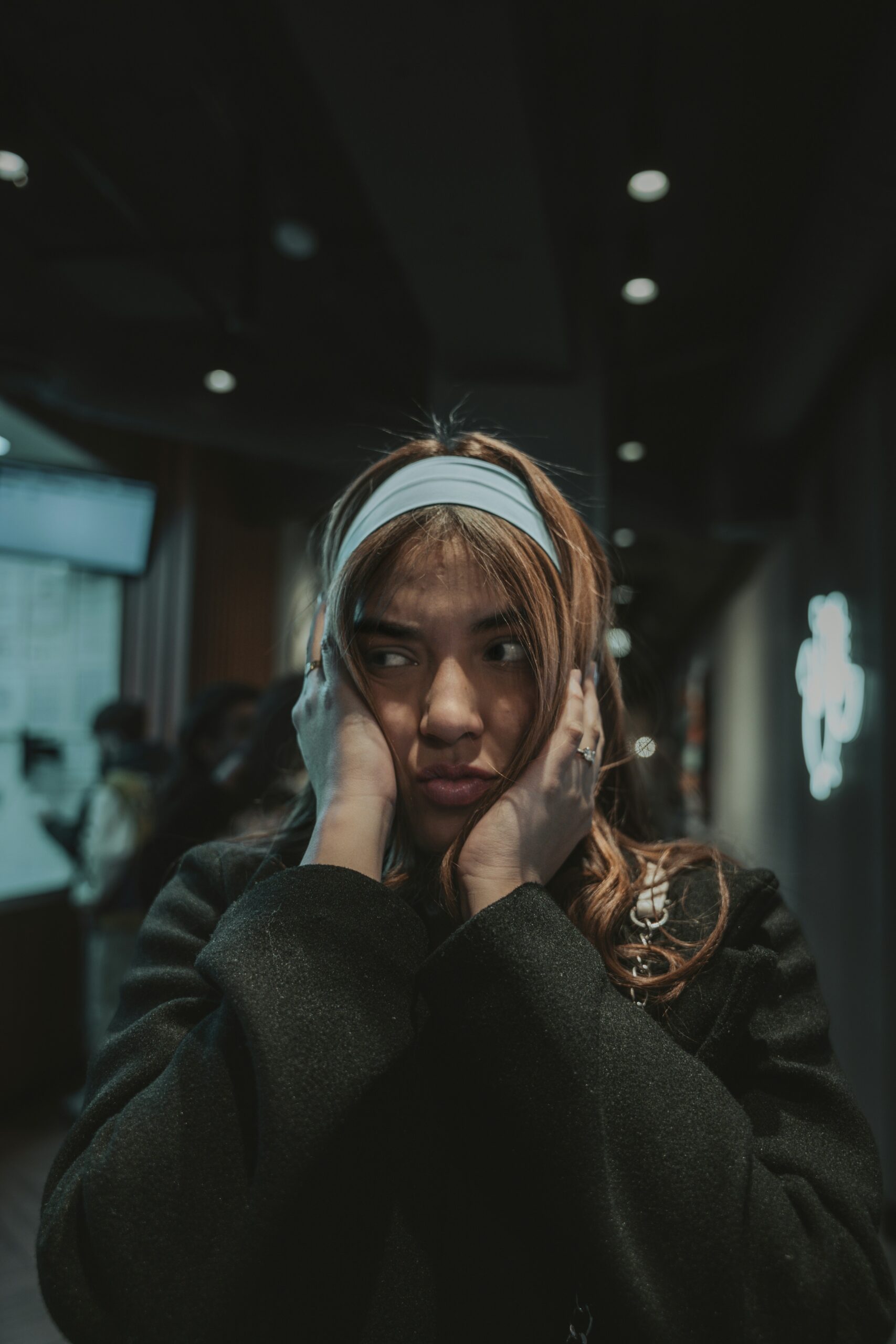 Young woman covering her ears in distress, possibly experiencing anxiety or emotional overwhelm in a public setting.
