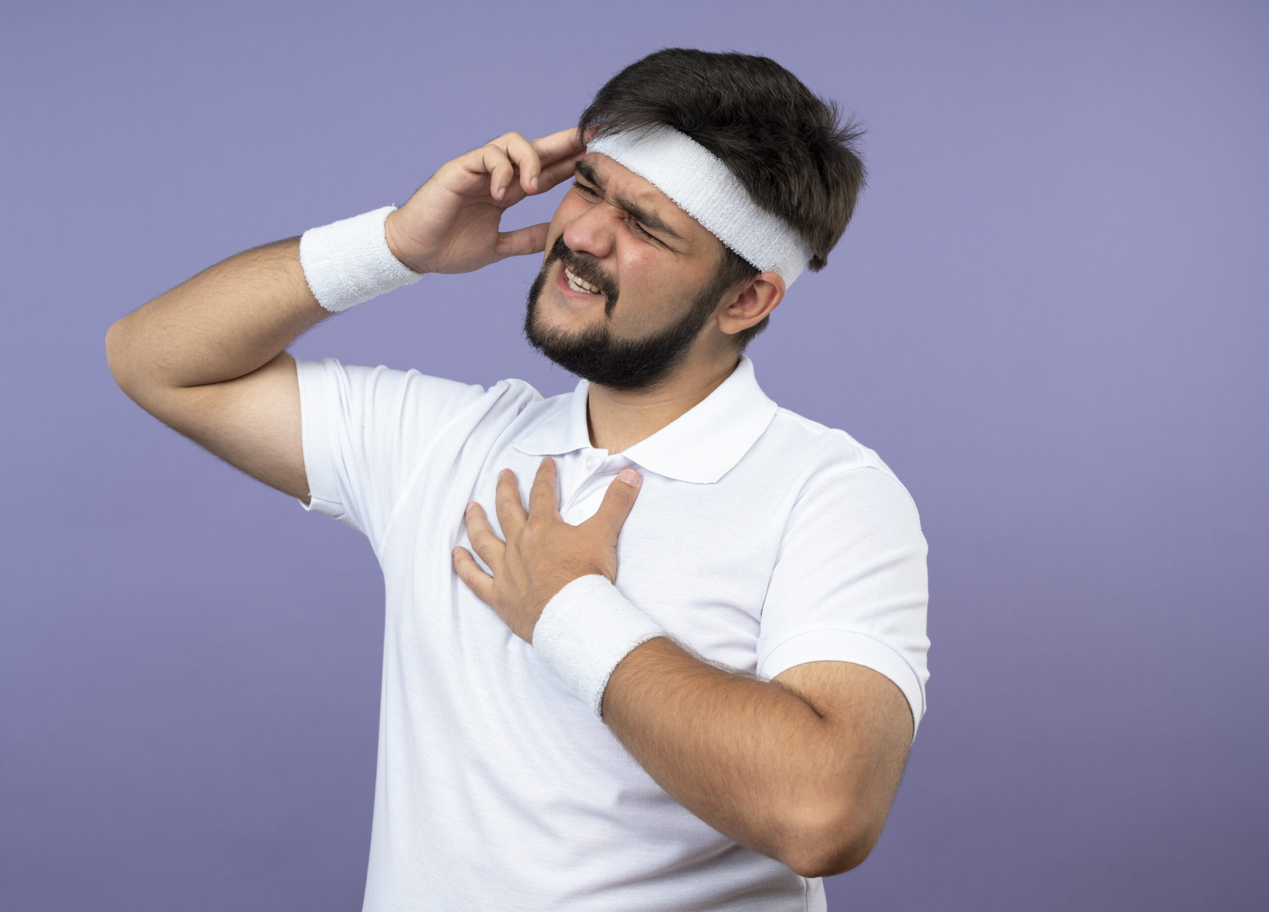 "Young man holding chest and head with painful expression, showing anxiety or cardiophobia symptoms"